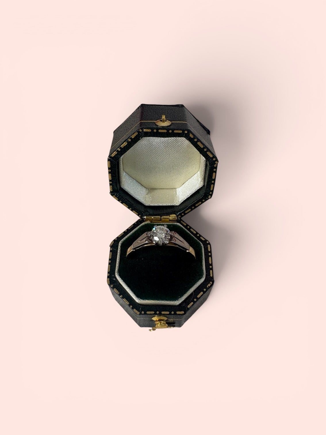 Black jewelry box with a transitional cut diamond solitaire ring inside on a light pink background
