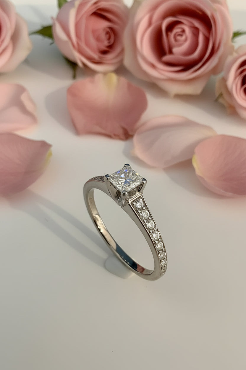 Canadian Maple Leaf Princess Cut diamond ethical Ekati Mine. white gold ring with a diamond on a white surface with pink flowers in the background