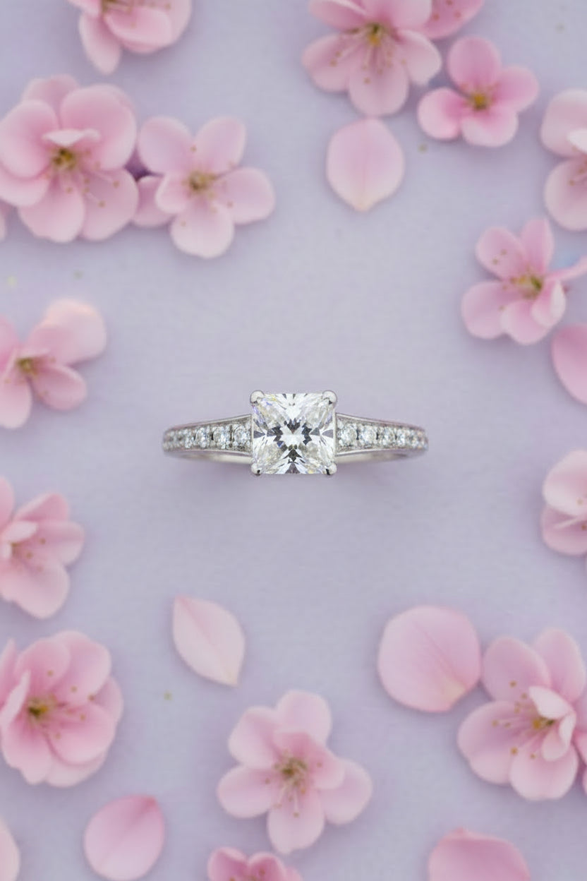 Silver ring with a princess cut diamond and smaller diamonds on a light gray background