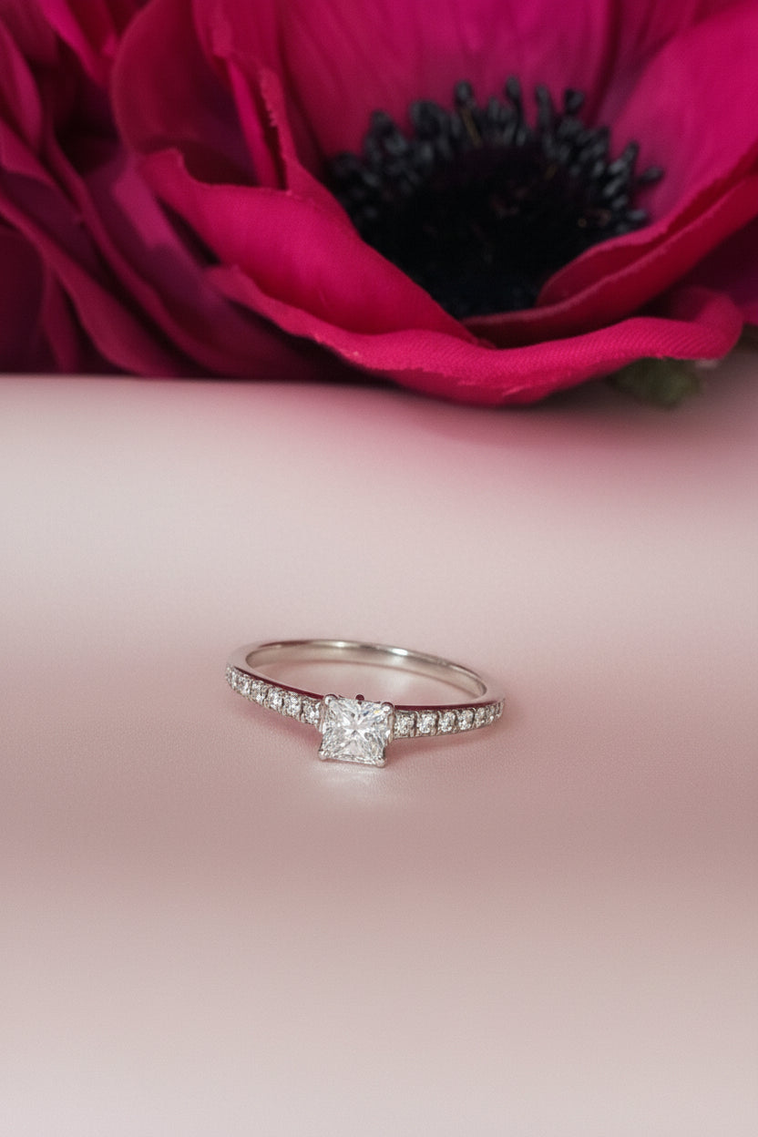 Silver ring with diamonds on a textured surface next to a pink flower