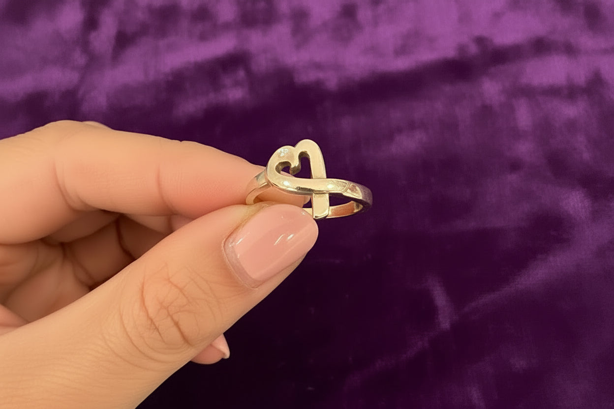 silver heart ring held between fingers against a purple textured background. Authentic Paloma Picasso Tiffany & Co. Loving Heart Ring