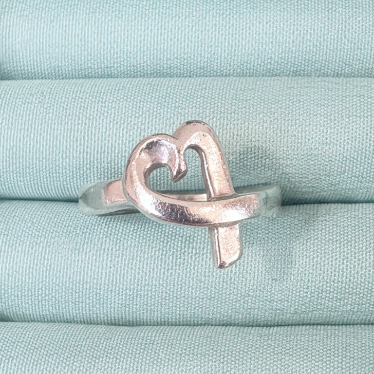 Silver ring with a heart design on a textured green fabric background