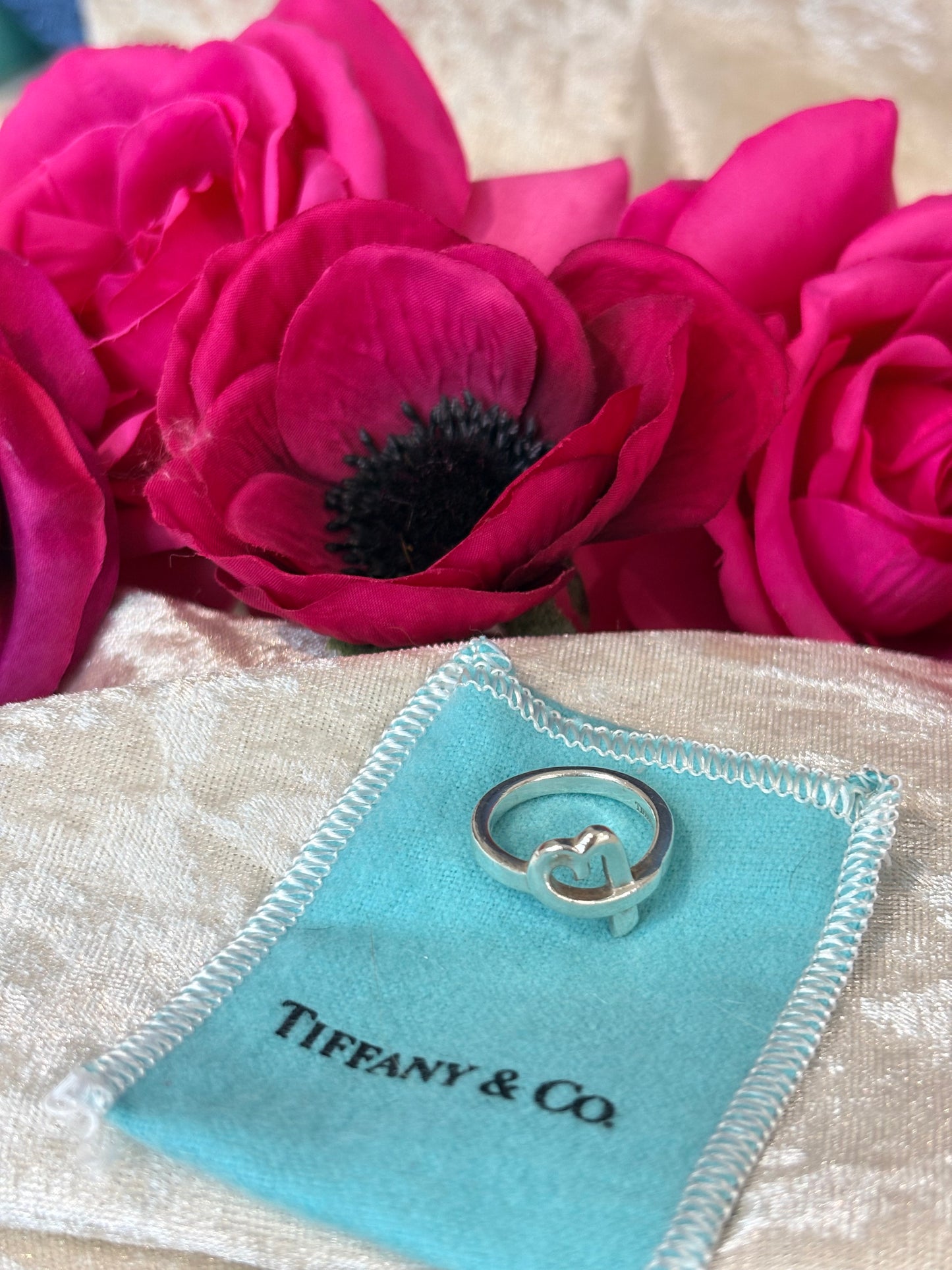 Tiffany & Co. ring on a blue jewelry pouch with pink flowers in the background