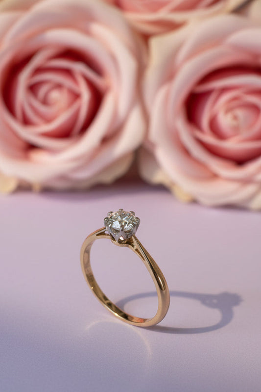 Gold ring with a diamond on a lilac serface with pink roses in the background old eaurpoean cut diamond solitaire 