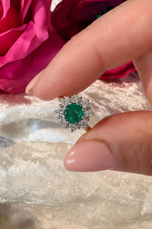 Hand holding a green gemstone ring with a pink flower in the background