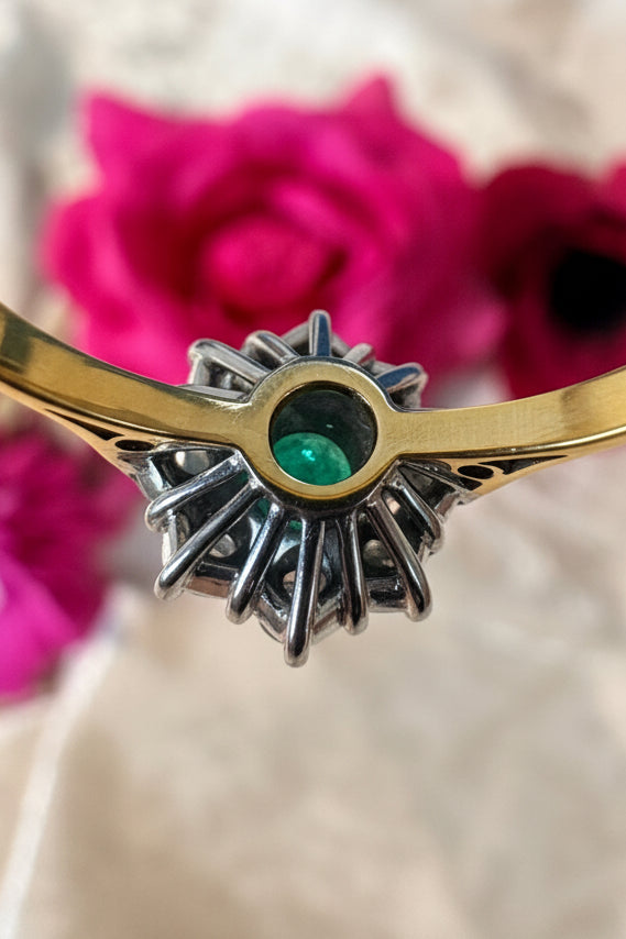 underside of the basket of emerald and gold ring on a blurred floral background