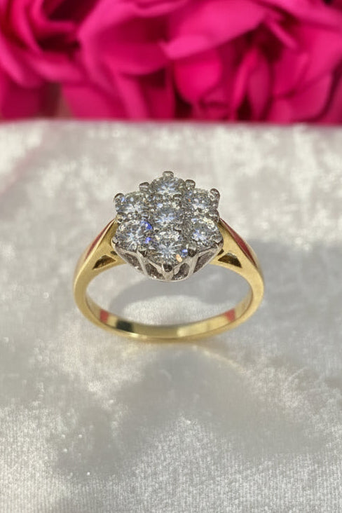 Gold dimaond daisy ring with 1ct of diamonds on a white surface with pink flowers in the background