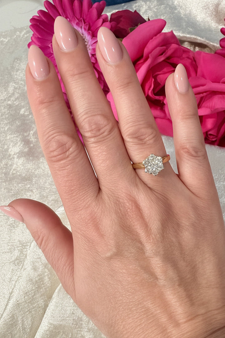 Hand wearing a daisy diamond ring with pink flowers in the background