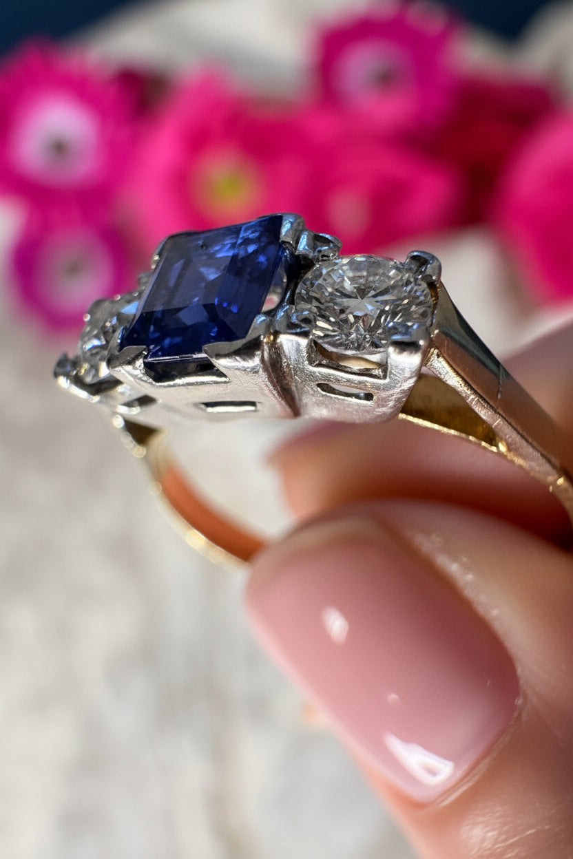 Close-up of a ring with a sapphire and two old European cut diamonds, held by a hand.