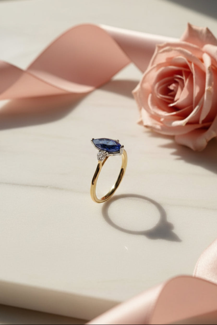 Gold ring with a blue sapphire and diamonds on a white surface