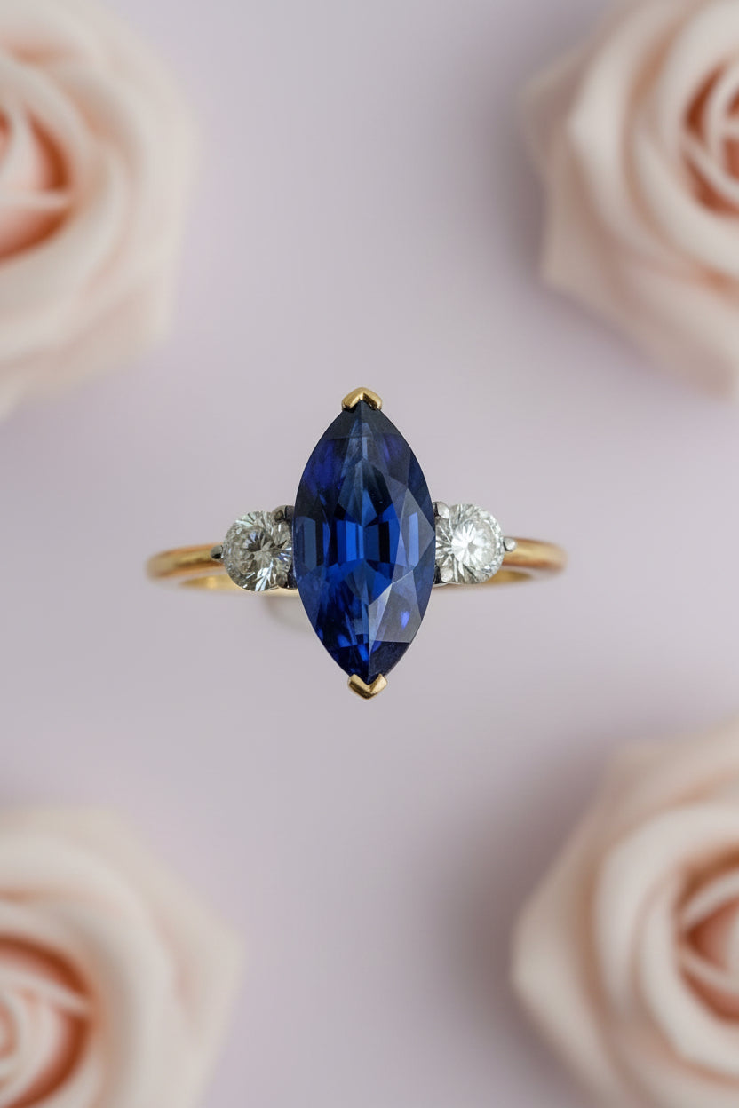 Gold ring with a blue sapphire and smaller diamonds on a pale background roses