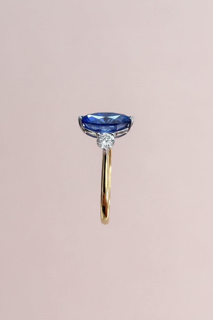 Side view of a gold ring with a blue sapphire held against a neutral background