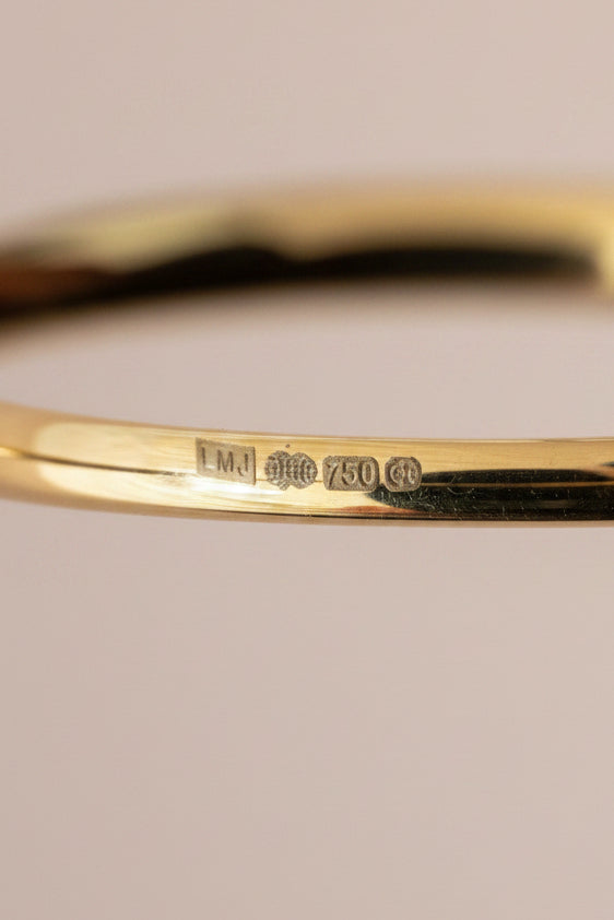 Close-up of a gold ring with hallmarks for 18ct gold and the Birmingham, UK assay office on a pale pink background