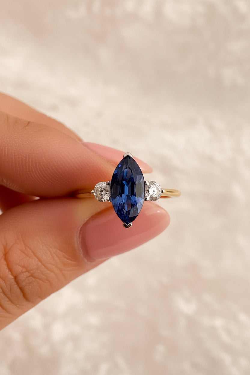 Blue sapphire ring held by a hand against a neutral background