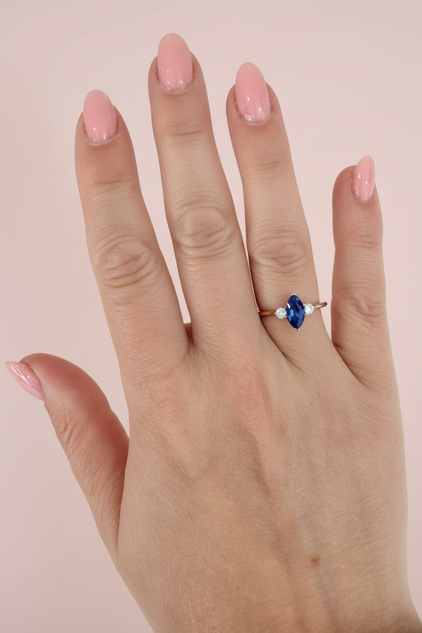 Hand wearing a ring with a blue sapphire on a textured pale pink background