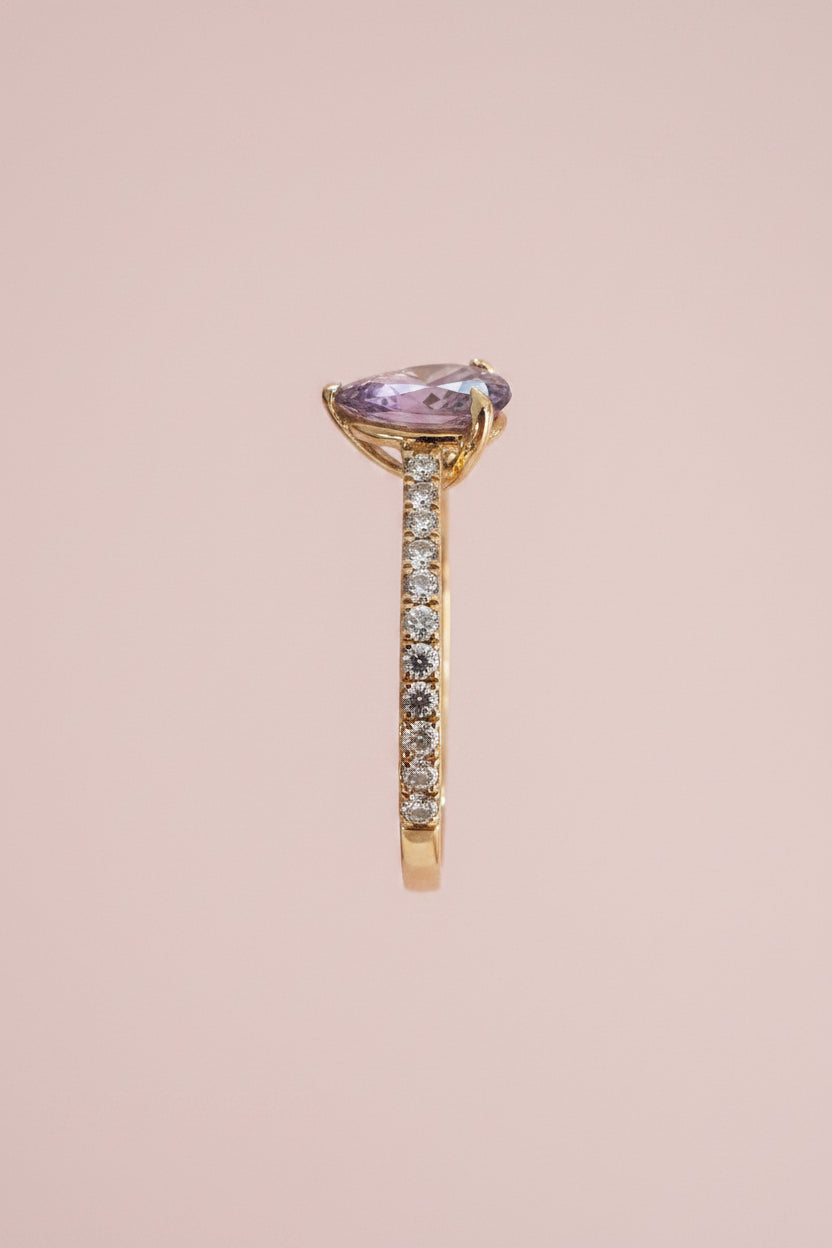 side view of a Gold ring with a brown sapphire and diamond shoulders against a pale pink background
