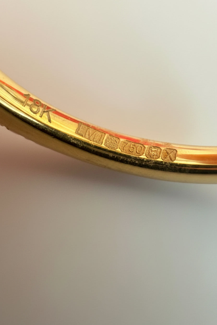 Close-up of a gold ring with full UK hallmarks and with '18K' marking on a light background