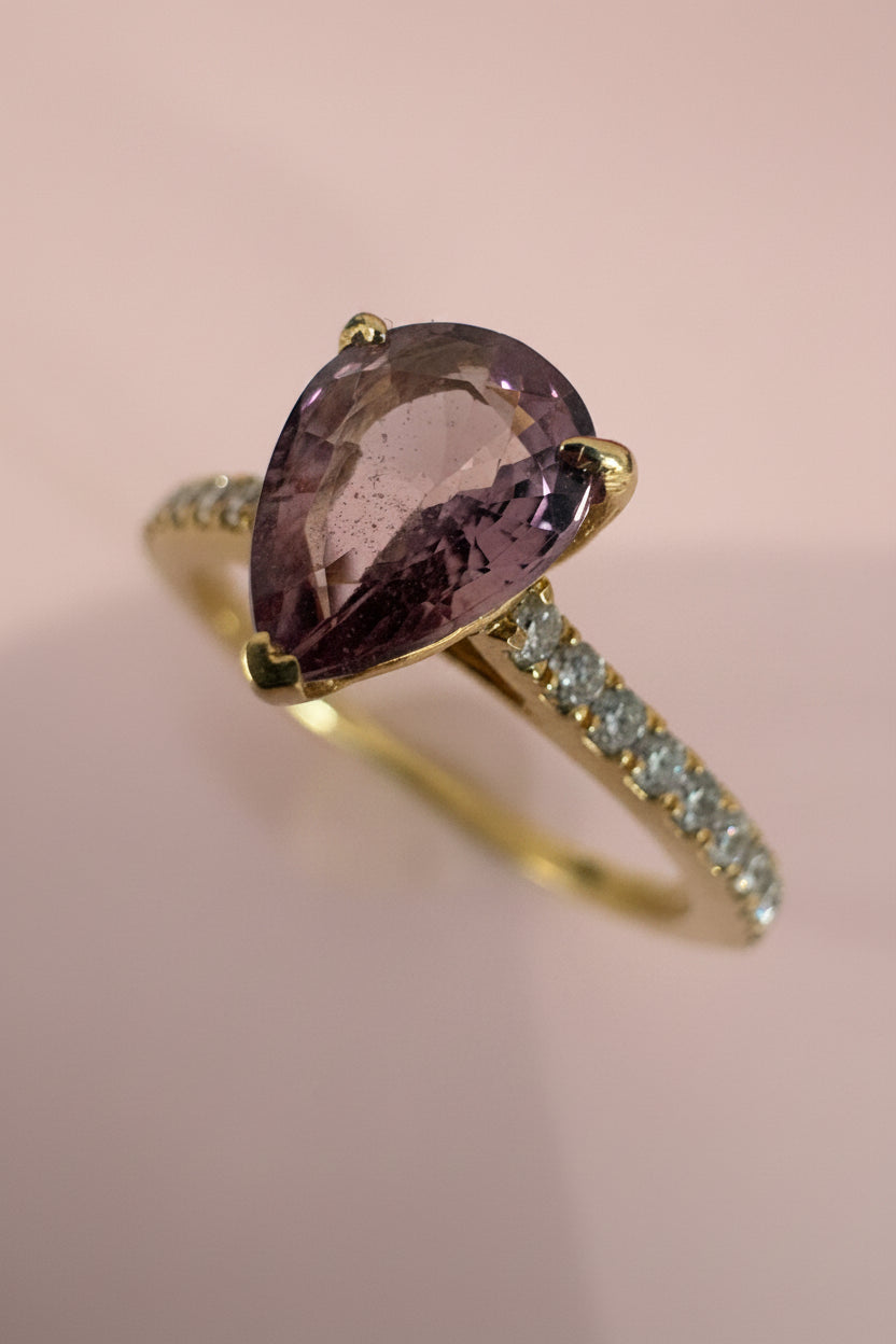 Gold ring with a brown sapphire and diamond accents on a light pink background