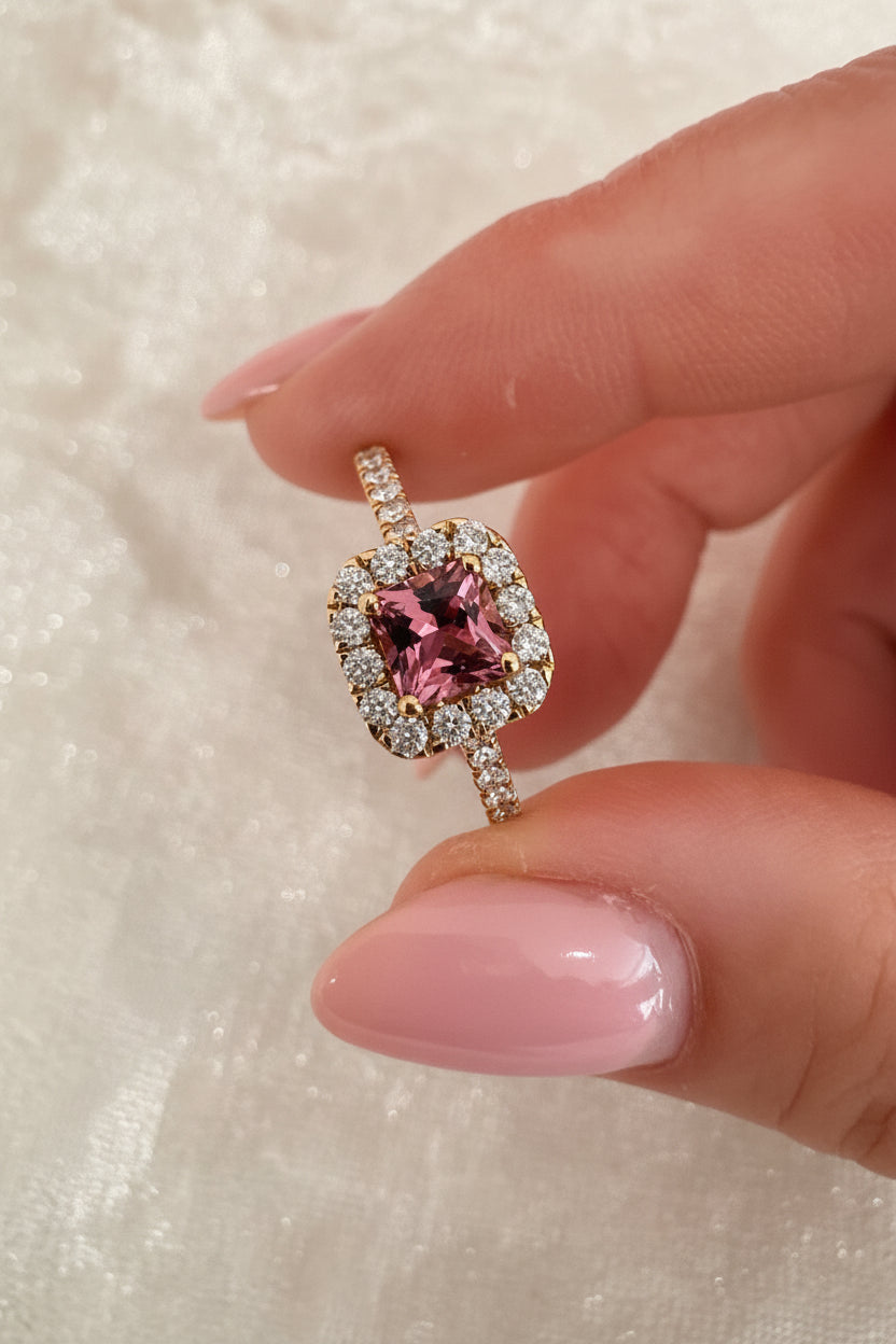 Ring with a pink tourmaline and diamonds held between fingers on a neutral background