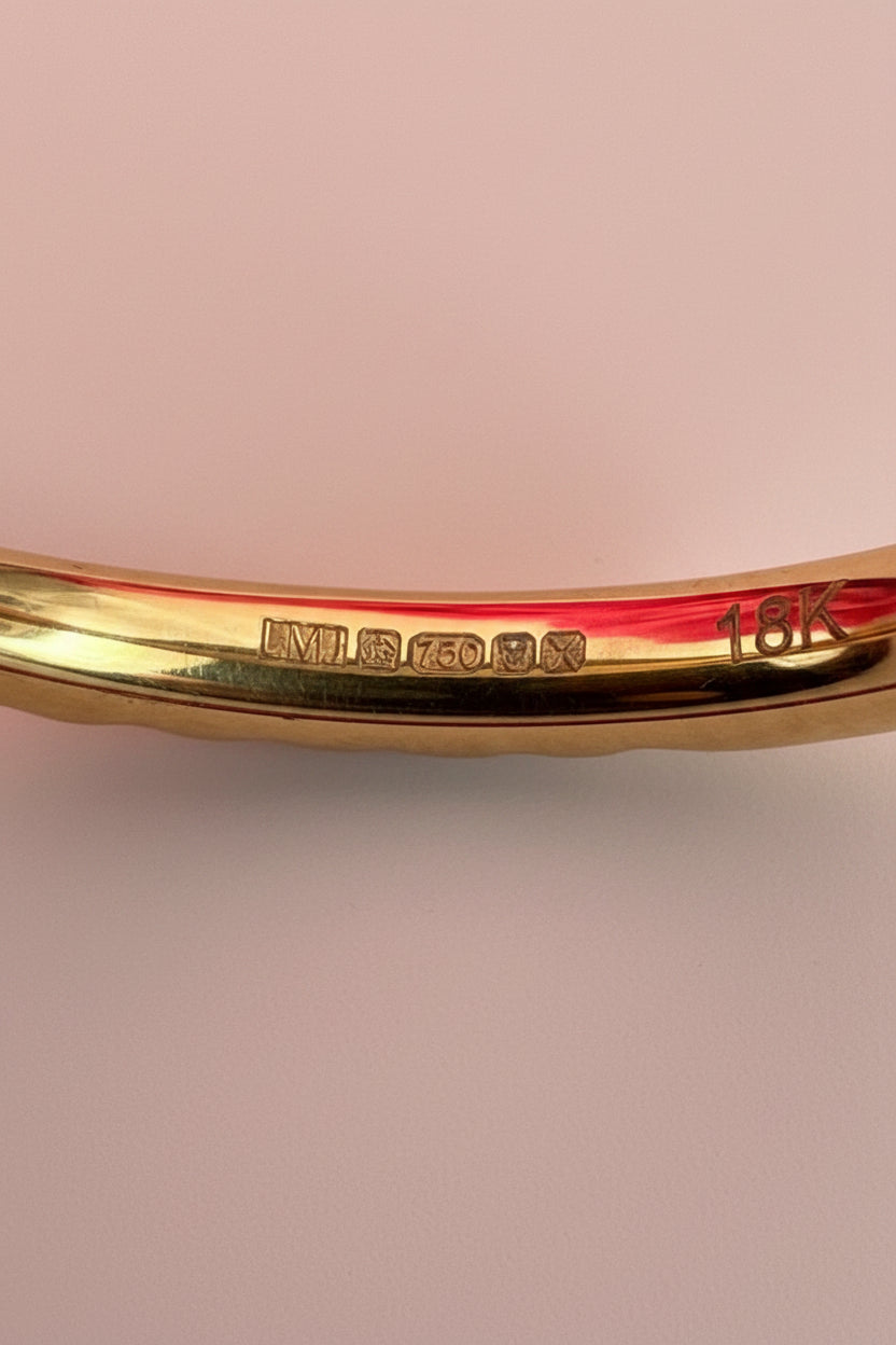 18ct London Assay mark with Gold crown, year stamp 'X' denoting 2021 and LMJ sponsors mark with '18K' marking on a gold ring on a pale pink surface