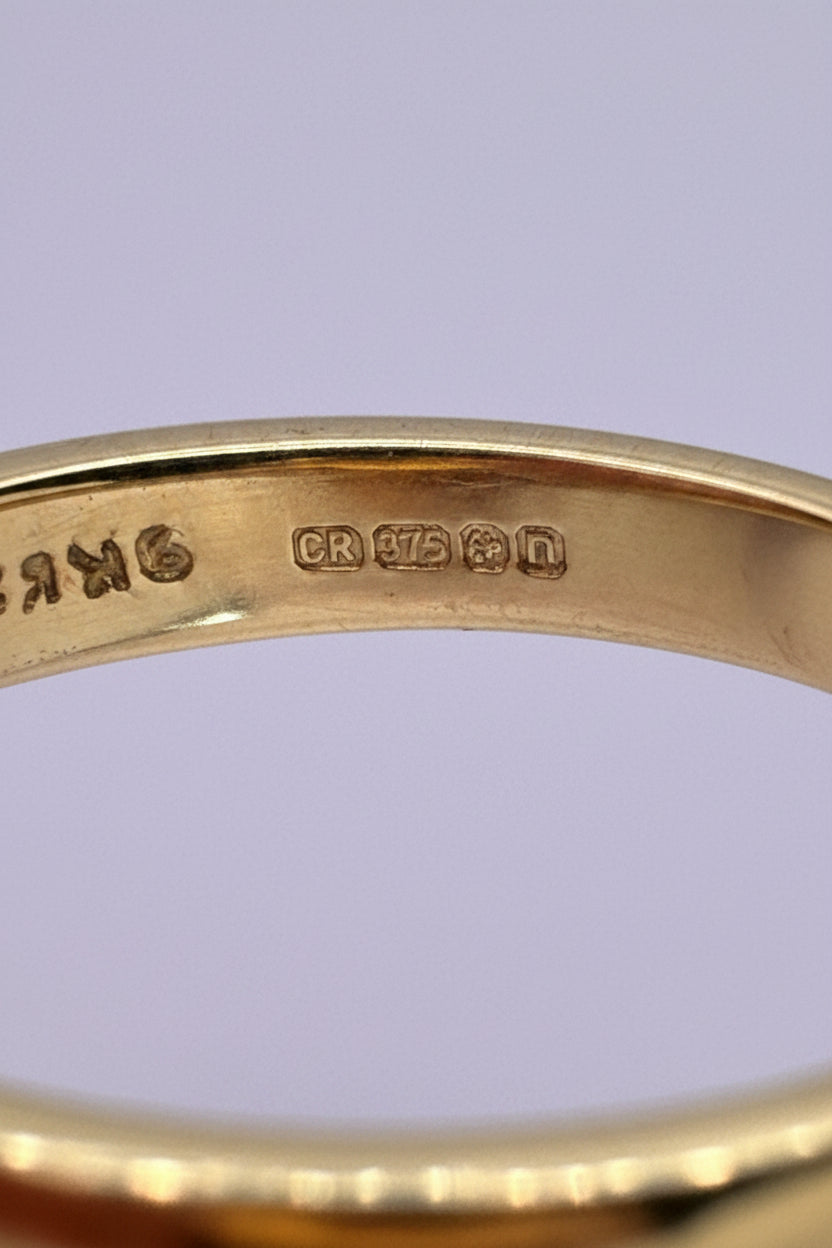 Close-up of the inside of a gold ring showing gold hallmarks, including 375 fineness mark and anchor for Birmingham assay office.