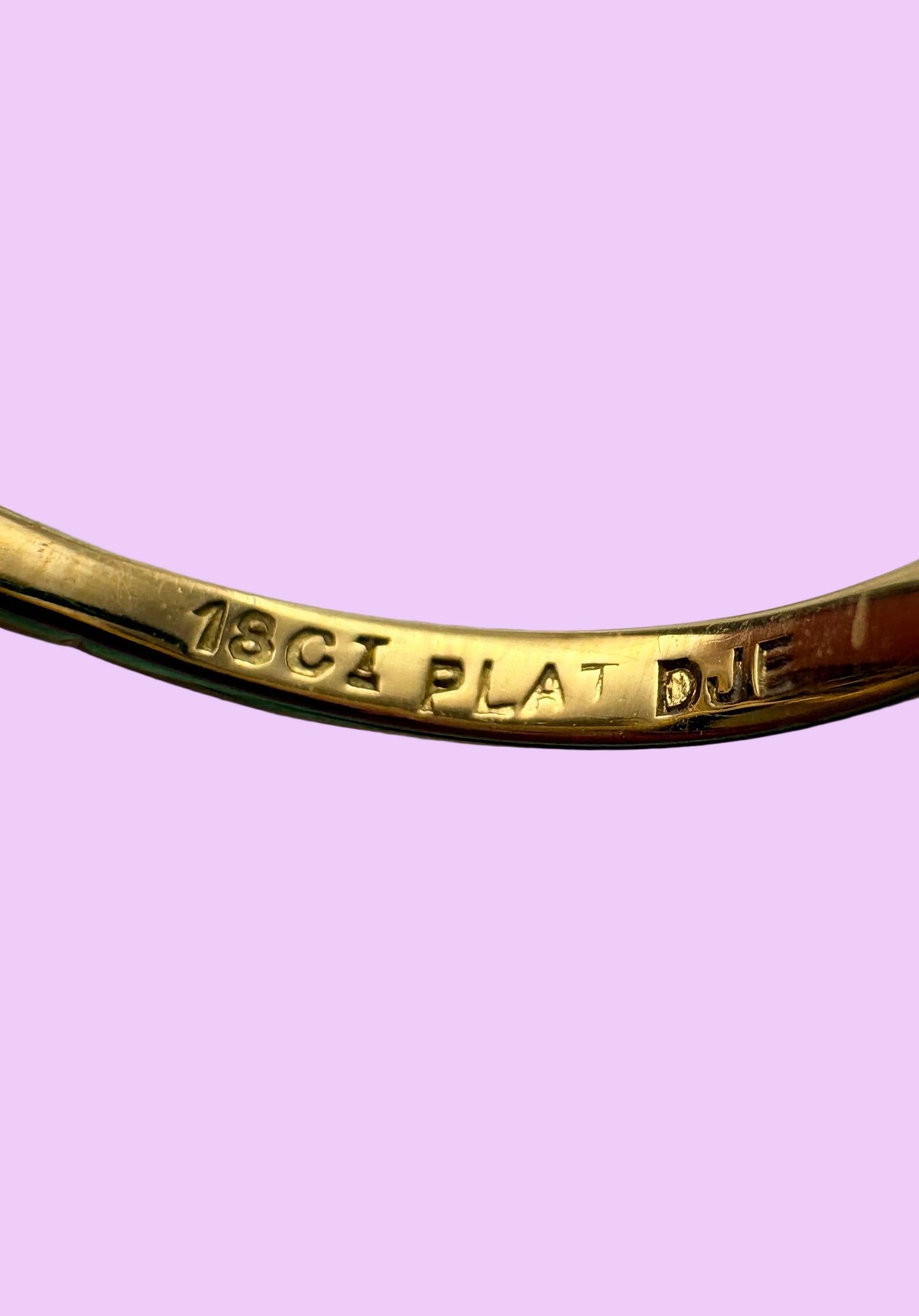 Close-up of a gold ring, showing the inner engraving '18CT PLAT DJE'.