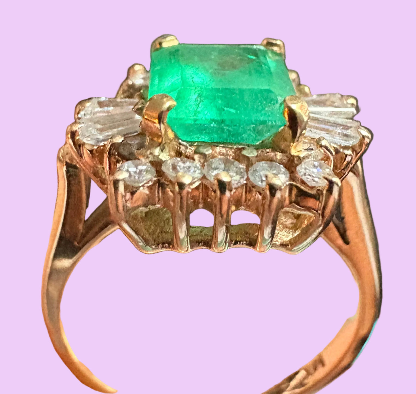 A yellow gold ring featuring a square-cut green emerald-cut gemstone in the center, surrounded by a halo of small clear round-cut and baguette-cut stones, set against a solid light purple background.
