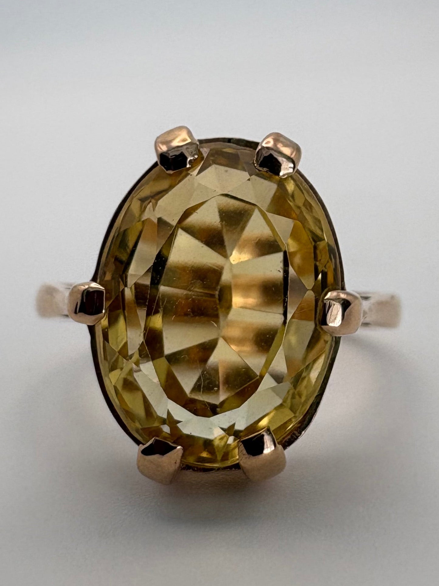 An oval-cut faceted gemstone ring in a gold-toned setting, photographed on a plain light gray background.