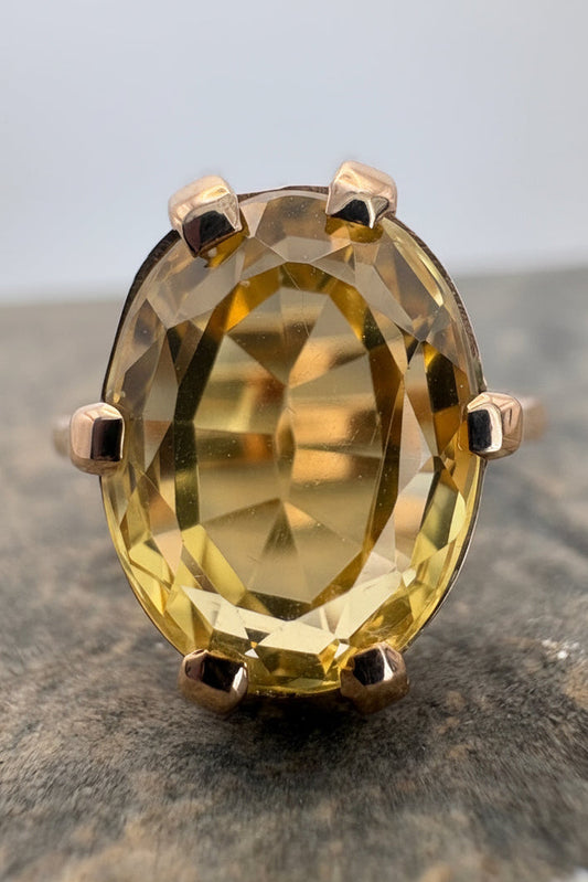 An oval-cut citrine gemstone ring set in a 9ct gold prong setting, resting on a textured gray stone surface.