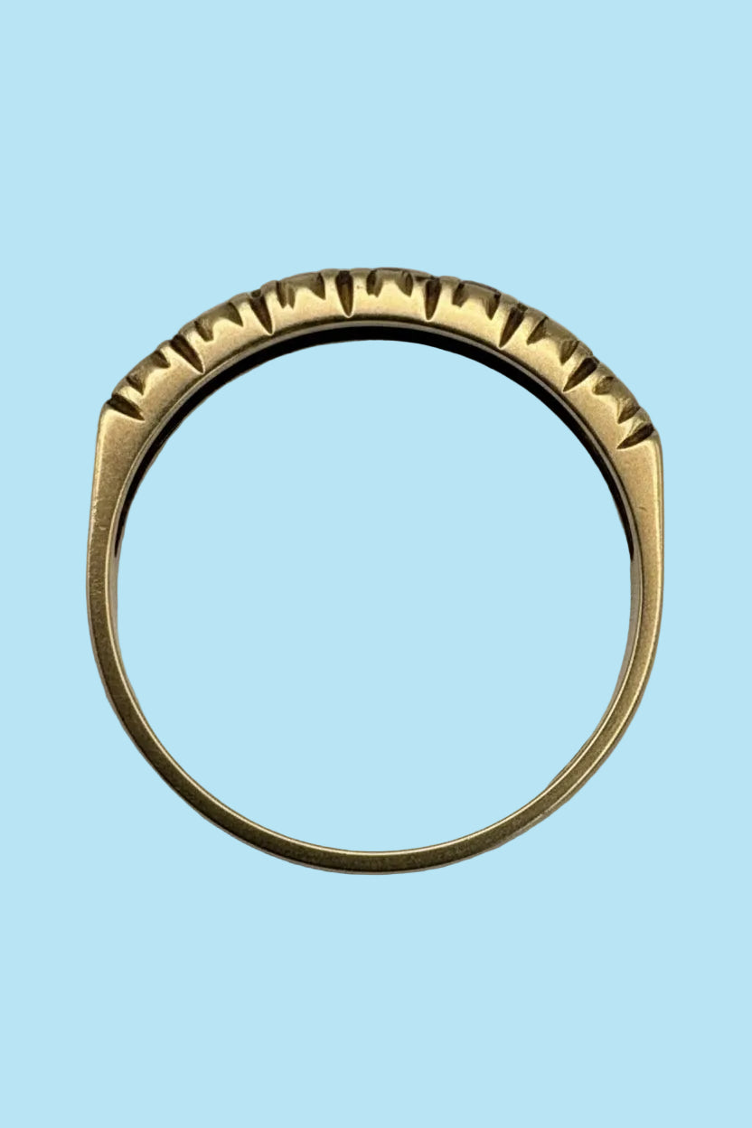 A gold ring with a textured, serrated outer edge, photographed on a plain light grey background.