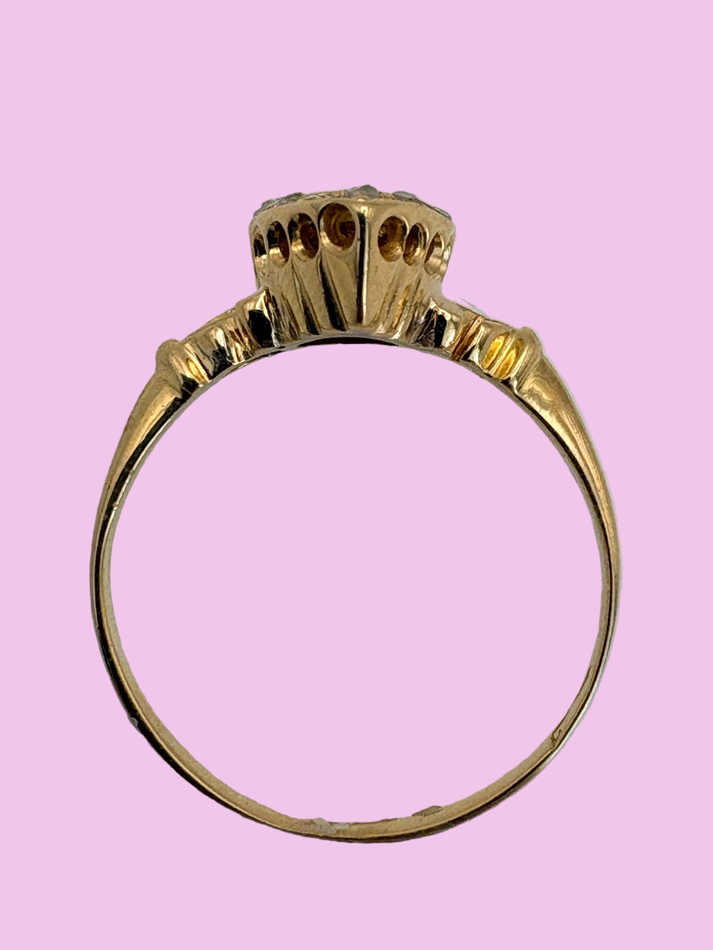 An antique yellow gold ring with a decorative crown-like top and a large oval center stone, photographed from above on a light purple background.