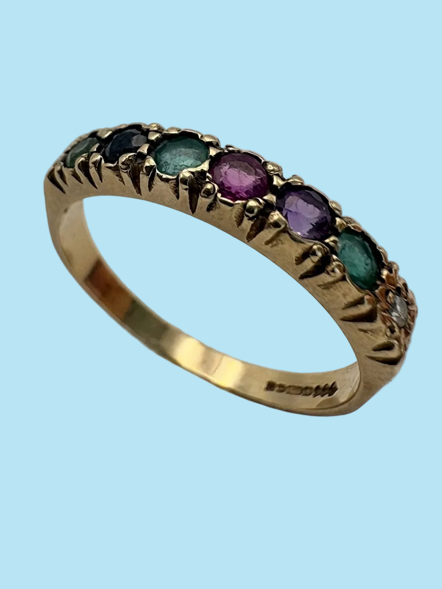 A yellow gold eternity ring featuring a row of round multicolored gemstones, including green, purple, and blue, set in a decorative patterned band.