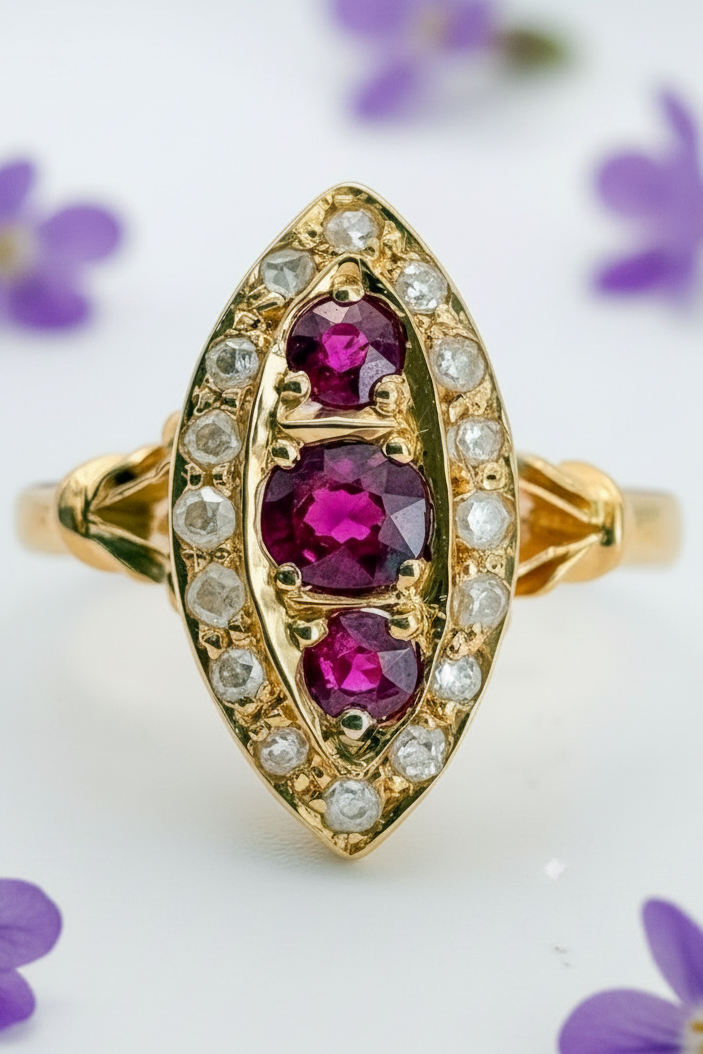 An antique gold ring featuring three oval-cut deep pinkish-purple rubies set in a gold marquise-shaped halo, surrounded by small round diamonds, on a white background.
